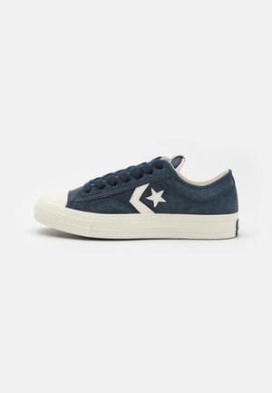 Niskie granatowe zamszowe sneakersy z białą gumową podeszwą, białą gwiazdą i logo w kształcie jodełki po boku oraz granatowymi sznurówkami, widoczne z lewej strony.