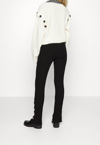 Vit texturerad tröja med svarta knappar på axlarna, i kombination med svarta ribbade byxor med sidoknappar. Svart fotgear fulländar outfiten.