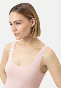 Bodysuit sans manches rose clair avec un col rond, texture lisse et sans motifs ni éléments visibles, conçu pour un aspect ajusté.