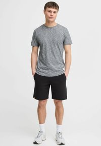 T-shirt en marle gris à manches courtes et col rond ; associée à un short noir. Modèle portant des chaussettes blanches et des baskets grises.