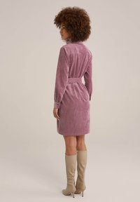 Rosa kordtklänning med långa ärmar och bälte i midjan, som har en krage och bakfåll, i kombination med beigefärgade knähöga stövlar.