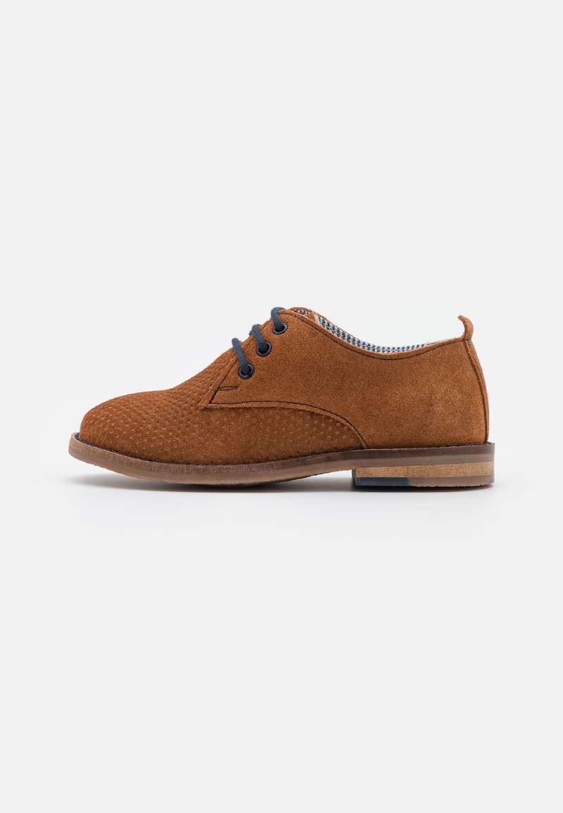 Chaussure oxford en daim marron avec devant texturé, lacets bleu marine, petit talon et doublure intérieure à carreaux, vue de côté sur fond blanc.