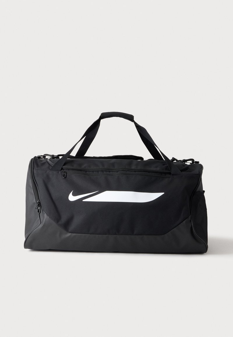 Μαύρη τσάντα duffel της Nike με διπλές λαβές, πλαϊνή τσέπη από δίχτυ και μεγάλο λευκό λογότυπο Swoosh στο μπροστινό μέρος με απλό φόντο.