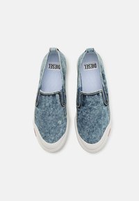 Denim-Slipper mit einer hellblauen Waschung. Weiße Gummisohle, blaue Innenauskleidung und minimalistisches Design mit kontrastierenden Nähten.
