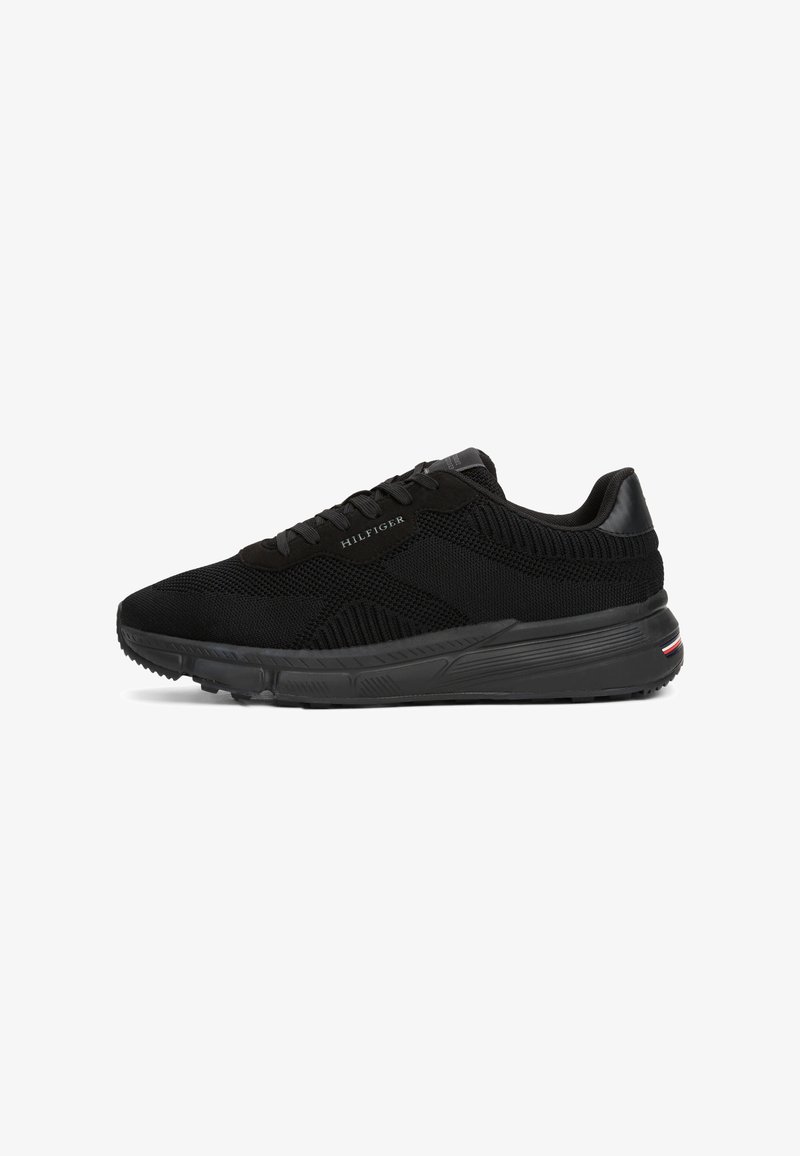Black athletic sneakers with a breathable mesh upper, textured accents, and a contrasting rubber sole featuring a multicolored stripe at heel.