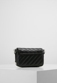 Borsa a tracolla nera in pelle trapuntata con chiusura a patta e hardware in argento, esposta su un piedistallo bianco su sfondo neutro.