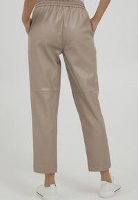 Beige faux leren broek met een elastische tailleband, cropped lengte en zijzakken, gecombineerd met witte sneakers.