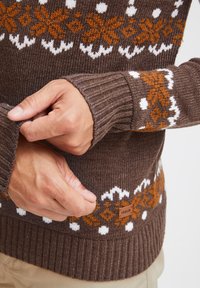 Jersey marrón de punto con un patrón geométrico en blanco y naranja. Puños y dobladillo acanalados. Pequeña etiqueta de cuero en el dobladillo inferior.
