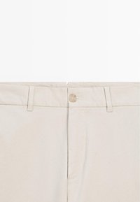 Pantalon beige vue de face montrant le bouton, les passants de ceinture et la braguette à glissière sur fond blanc uni.