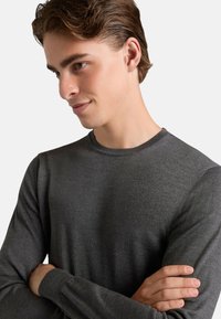 Maglione grigio a maniche lunghe in tessuto a maglia fine con scollo rotondo. Presenta una vestibilità aderente e dettagli a coste sui polsini.