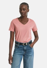 Roze v-hals t-shirt gemaakt van zacht materiaal, met korte mouwen, gecombineerd met hoge taille denim jeans met een zwarte riem en zilveren gesp.
