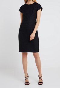 Czarna sukienka z fakturowanej tkaniny, o przyległym fasonie, z krótkimi rękawami typu cap i długości do kolan. Podkreślona subtelnymi wzorami.