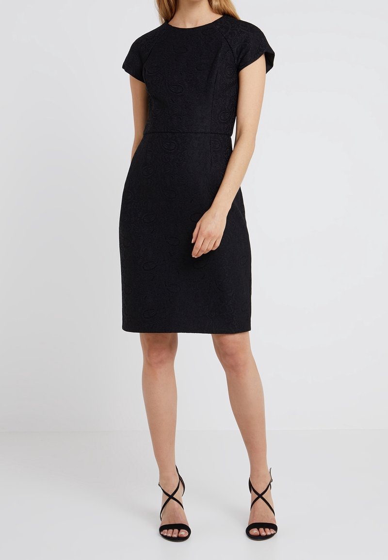 Czarna sukienka z fakturowanej tkaniny, o przyległym fasonie, z krótkimi rękawami typu cap i długości do kolan. Podkreślona subtelnymi wzorami.