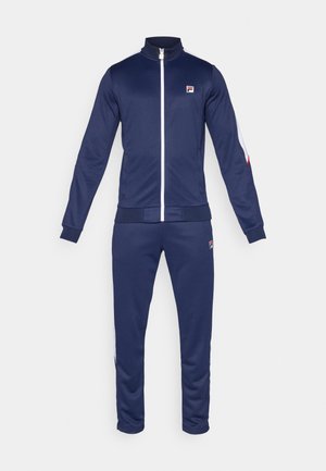 Chándal azul marino hecho de tejido suave, con cuello alto, cremallera completa y acentos blancos en las mangas; parche de logo en el pecho y la pierna.