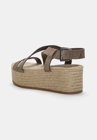 Braune Wildleder-Wedge-Sandale mit einer geflochtenen Jute-Plattform, verstellbarem Knöchelriemen und einem runden Zehendesign. Minimalistischer Stil mit klaren Linien.