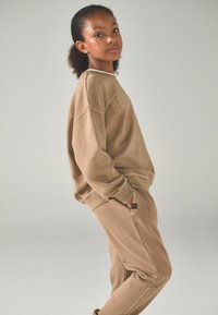 Tann sweatshirt och matchande sweatpants i mjukt tyg; har rund halsringning och ribbade ärmslut, med logotypdetalj på framsidan.