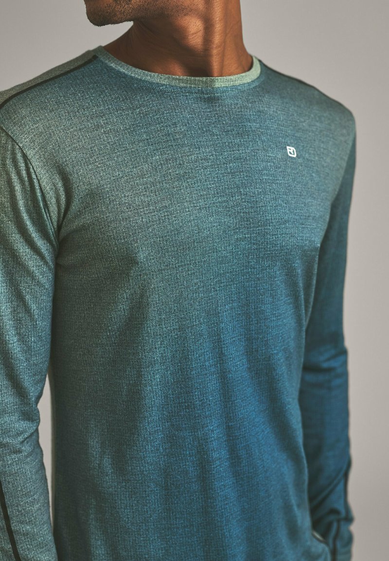 Long-sleeve shirt in gradient teal fabric, featuring a textured pattern, round neckline, and subtle logo on the chest. Accented with black shoulder seams.