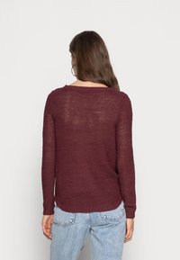 Pull en maille bordeaux à manches longues, col rond et motif texturé, avec une coupe décontractée et un ourlet arrière légèrement plus long.