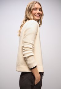 Vaalean kermainen collegepaita rentoutuneella istuvuudella, resorit hihansuissa ja helmassa. Varustettu teksturoidulla kankaalla ja sivutaskuilla, yhdistetty tummiin housuihin.