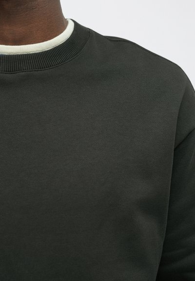 Ciemnozielona bluza z ribbowym okrągłym dekoltem i teksturowanym materiałem. Projekt jest prosty, nie posiada widocznych wzorów ani metalowych akcentów.