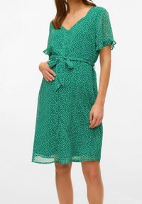 Vestido verde con lunares, hecho de una tela ligera, que presenta mangas cortas con vuelo, un escote en V y un detalle de lazo en la cintura. Falda con un corte fluido.