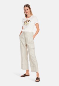 Weißes T-Shirt mit buntem Blumenmotiv, kombiniert mit hellbeigen, weit geschnittenen Cargo-Hosen mit seitlichen Taschen und einem strukturierten Saum.