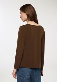 Maglietta marrone a maniche lunghe con scollo rotondo, realizzata in tessuto morbido. Presenta una vestibilità dritta e fessure laterali, abbinata a pantaloni in denim blu.
