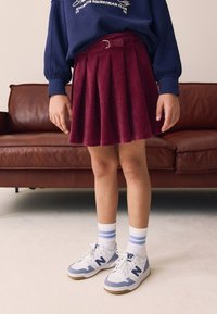 Gonna plissettata in velluto a coste color marrone con dettaglio cintura, abbinata a calzini bianchi e blu a righe e sneakers bianche con accenti viola.