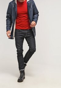 Marineblå vandtæt jakke med sherpa-foring, rød t-shirt, mørke jeans og sorte ankelstøvler, der viser et afslappet, lagdelt outfit.