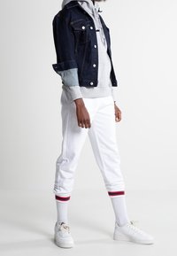 Chaqueta de mezclilla, sudadera gris con capucha, pantalones joggers blancos con franjas rojas y azules, zapatillas blancas. Ropa casual con texturas superpuestas y colores contrastantes.