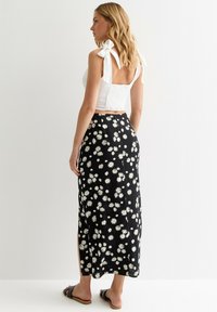 White cropped top with adjustable bow shoulder straps paired with a black floral maxi skirt featuring white daisy patterns and side slits.