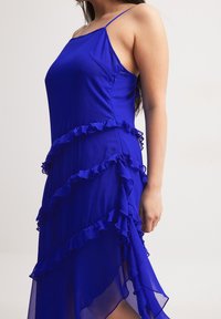 Blue, sleeveless dress with ruffled tiers and a flowing texture. Features delicate straps and asymmetrical hemline, crafted from lightweight fabric.
