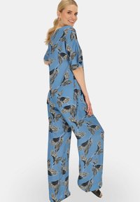Niebieski zestaw lounge składający się z luźnej bluzki i szerokich spodni, zdobiony czarno-białymi wzorami ptaków i liści, wykonany z gładkiego materiału.