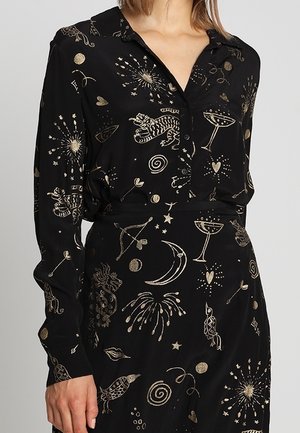 Schwarzes Langarmshirt und Rock mit goldenen, himmlischen und tierischen Mustern, darunter Monde, Sterne, Tiger und Cocktails, getragen von einer Person.