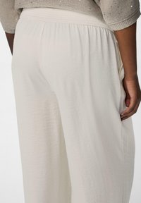 Pantaloni a palazzo color crema con un tessuto testurizzato, dotati di una vita elastica e tasche laterali, mostrati di spalle.