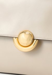 Bež usnjena torbica z okroglim zlato zaponko, na kateri je vgravirano "FURLA", na poklopni zaponki.