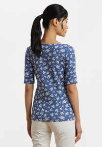 Camicia a maniche corte blu navy con motivo floreale bianco, scollatura tonda e design aderente. Materiale morbido, texture sottile e stile informale.