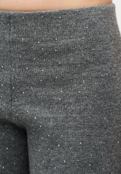 Κοντινό πλάνο σκούρων γκρί πλεκτών παντελονιών ψηλόμεσων με μικρές ασημένιες παγιέτες διασκορπισμένες στο ύφασμα.