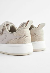 Beige Sneakers aus einer Mischung aus glattem und strukturiertem Wildleder, mit einer weißen Gummisohle und Stoffschlaufen an der Ferse für einfaches Anziehen.