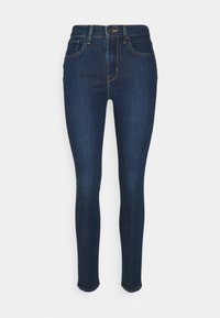 Jeans ajustados de denim azul oscuro, con una cintura alta, cinco bolsillos y detalle de costura dorada a lo largo de las costuras.