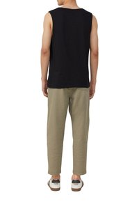Zwarte mouwloze top, licht olijfgroene relaxed-fit broek en witte sneakers met zwarte accenten. Zichtbare naden, casual ontwerp en zachte texturen.