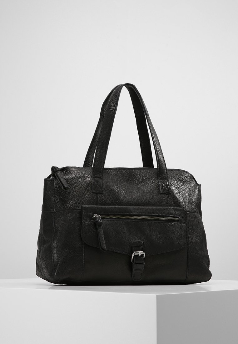 Sac à main en cuir noir texturé avec deux anses, poche zippée avant avec rabat et boucle, exposé sur un socle blanc sur un fond uni.