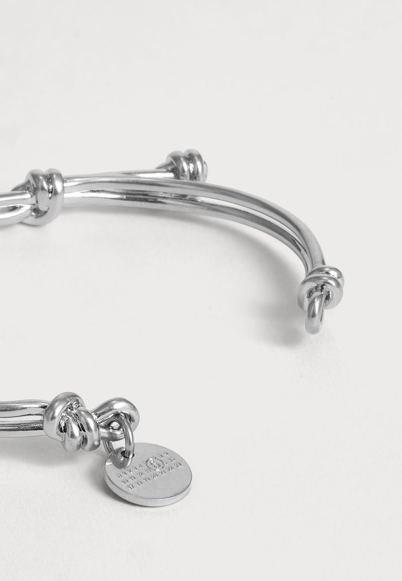 Zilveren armband met geknoopte details en een ronde gegraveerde bedel, weergegeven op een effen witte achtergrond.