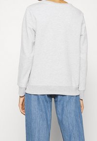 Sudadera gris con escote redondeado y puños acanalados, con una textura suave. Combinada con jeans de pierna ancha azul, todo en un estilo casual.