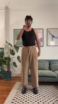Black tank top, beige corduroy wide-leg pants with front pockets, worn with black shoes; indoor setting, green plant in the background.