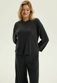 Czarny zestaw odzieży domowej składający się z długiego rękawa i luźnych spodni. Materiał jest gładki i miękki, a sylwetka jest swobodna.