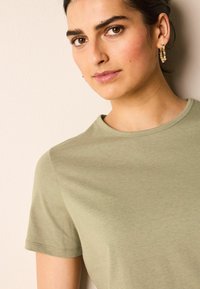 Camiseta de algodón verde oliva con cuello redondo, mangas cortas y una textura suave, con detalles de costura sutiles.
