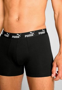 Black boxer briefs with a soft texture, featuring a thick elastic waistband with white "PUMA" logo and branding for support and comfort.