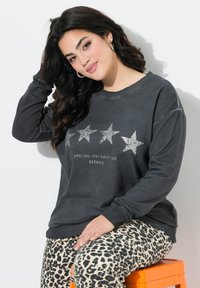 Felpa grigia con cinque stelle argentate e testo "BROWNIE". Abbinata a pantaloni beige con stampa leopardata. Il tessuto sembra morbido e casual.