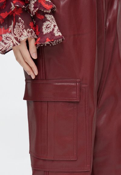 A bordó bőr nadrág nagy oldalzsebbel rendelkezik, lapos szélekkel. A textúra sima, fényes felülettel, amit virágmintás ujj egészít ki.